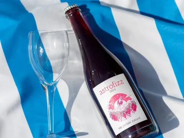 The bottle of astrofizz lying on a blue-and-white striped tablecloth, next to an empty glass