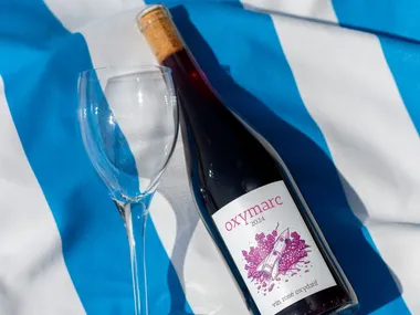The bottle of oxymarc lying on a blue-and-white striped tablecloth, next to an empty glass