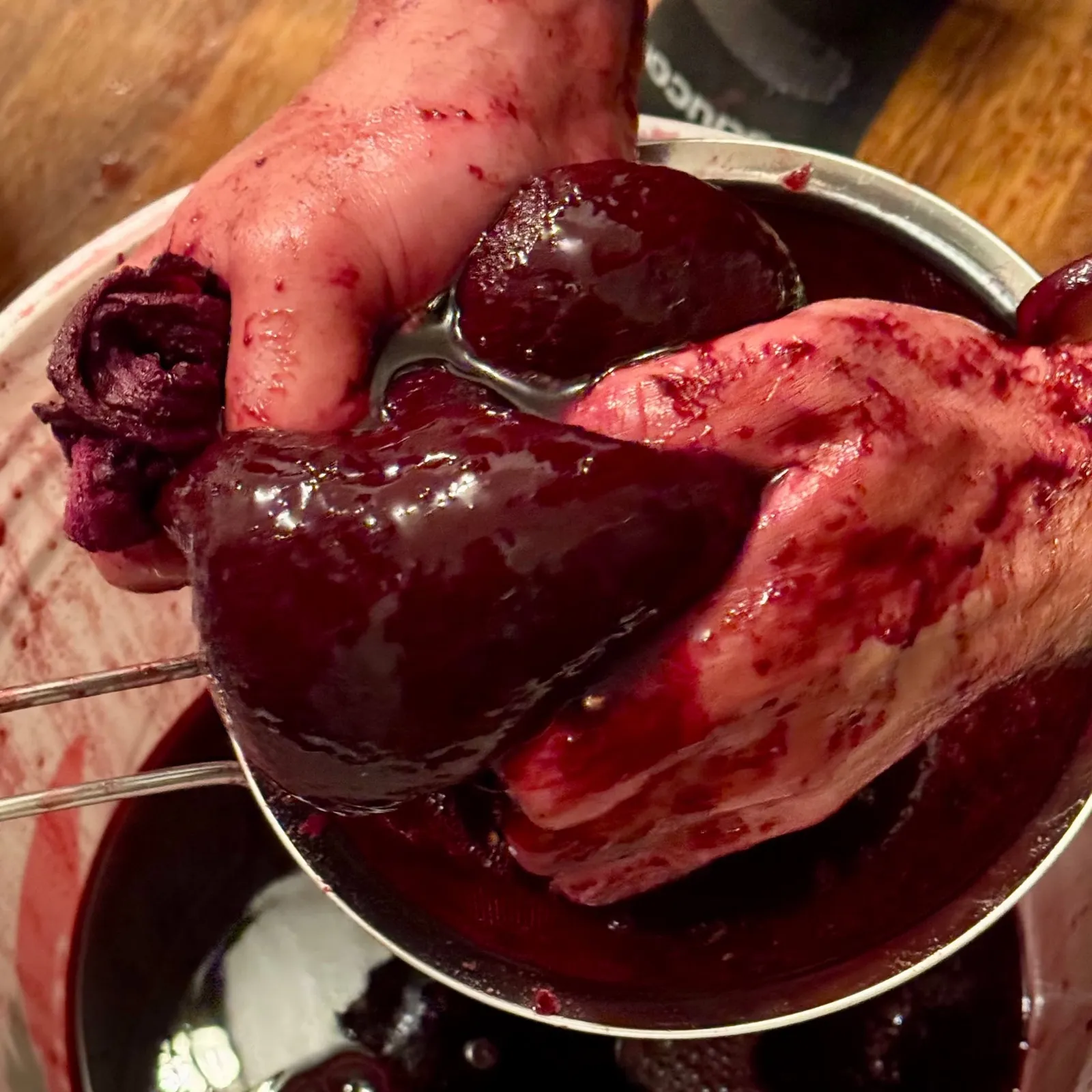 Hands pressing red grape solids in a strainer: the fine solids pass through any household filter
