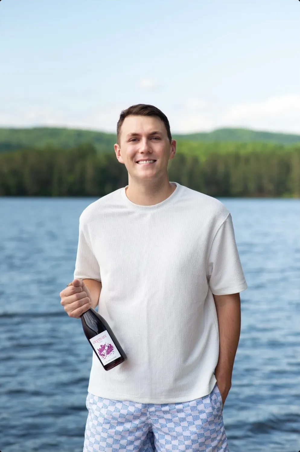 Samuel, souriant au bord d’un lac, une bouteille à la main