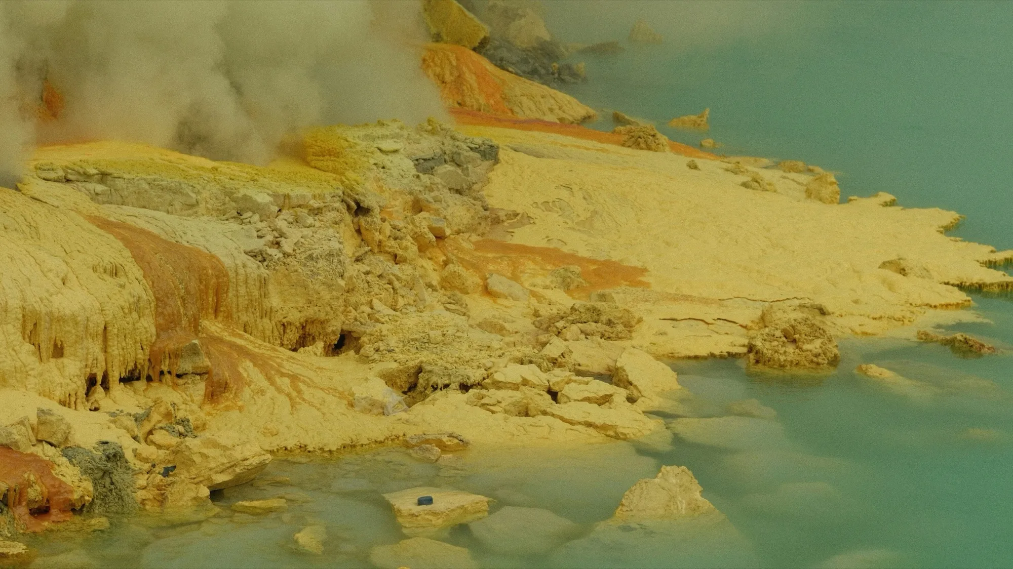 Yellow and orange native sulphur wrapped in steam, beside turquoise water